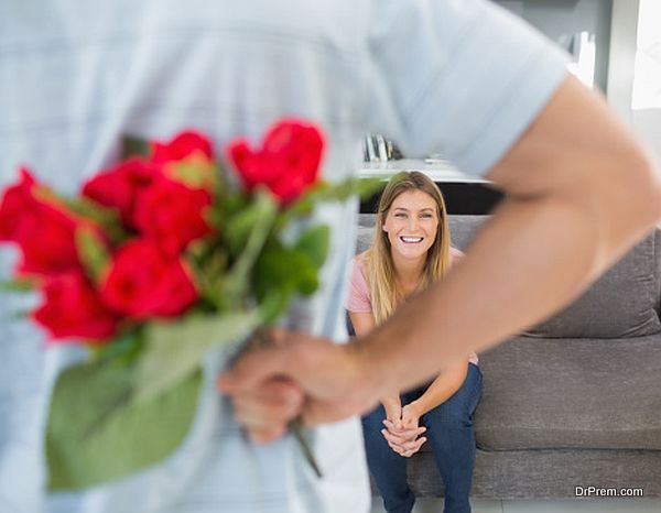 Man hiding bouquet of roses from girlfriend on the couch