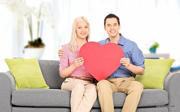 Young couple sitting at sofa and holding big red heart