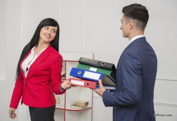 Side view of business man with folders flirting in office with his colleague with pretty smile in red jacket looking at him, with copy space on the wall